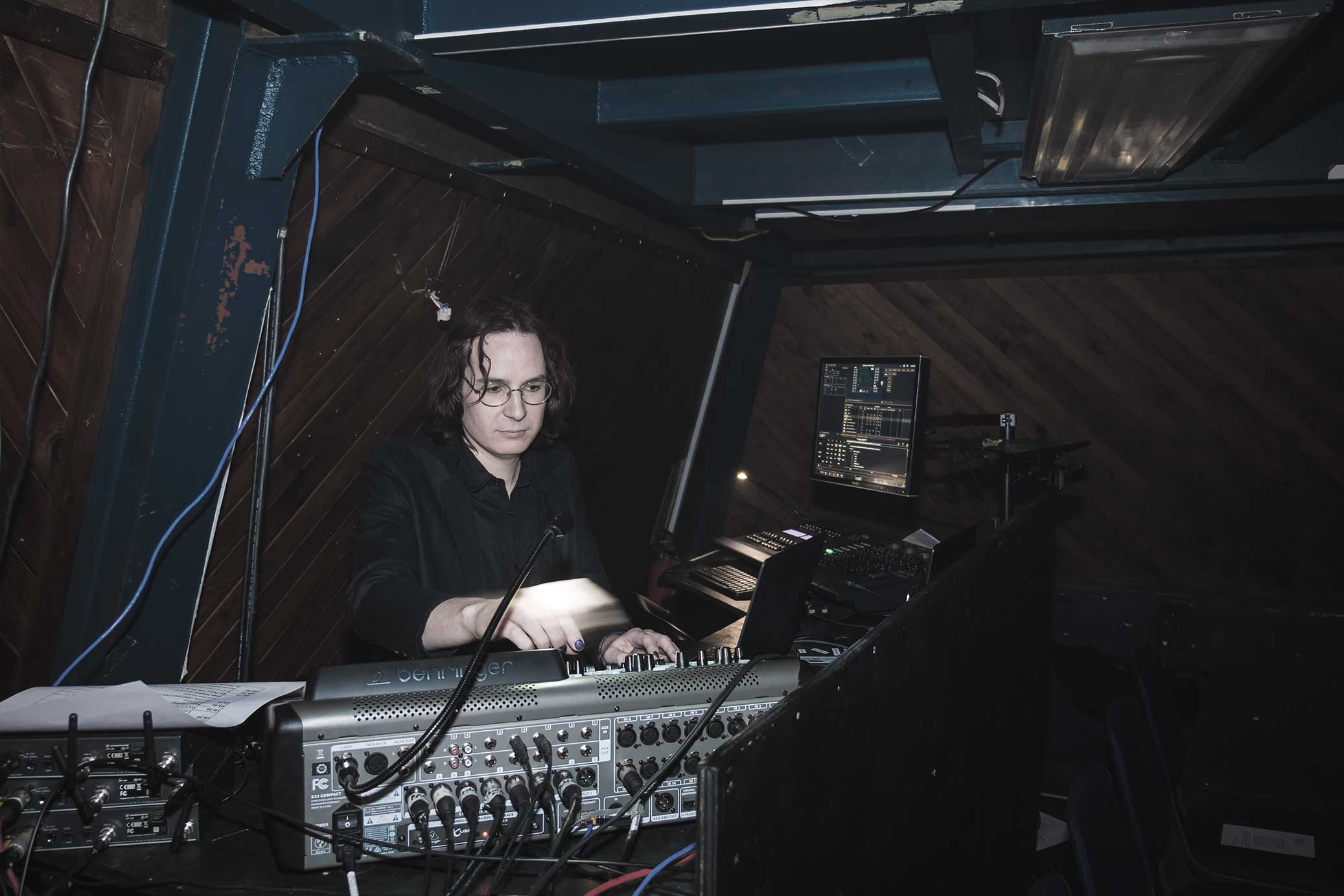 Photo of Paige smiling at the camera while operating a sound console.